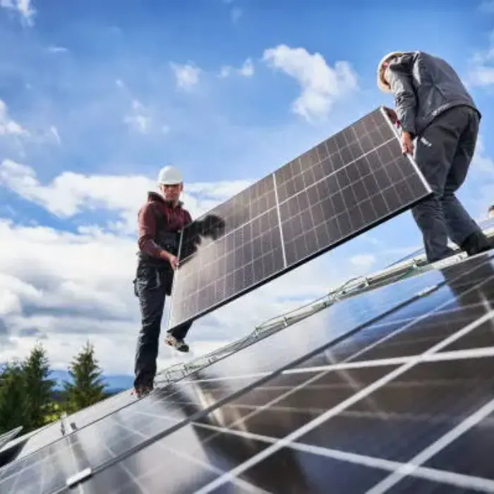 Dos técnicos de Gestión inversión con cascos de seguridad instalando un panel solar fotovoltaico en un tejado inclinado.