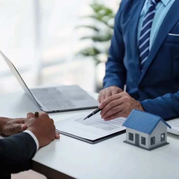 Un cliente firma un acuerdo inmobiliario mientras un asesor de Gestión inversión le señala los puntos clave del documento para garantizar su comprensión.