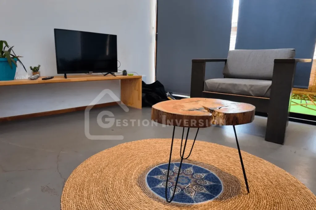 El cuidado diseño interior de una casa en Algarrobo, donde detalles como la mesa de centro rústica y el sillón moderno crean un ambiente acogedor, una característica de las casas de Gestión inversión.