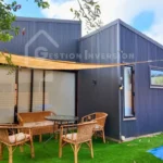 Un acogedor rincón exterior con muebles de terraza y césped artificial, que complementa el diseño industrial de esta casa en venta de Gestión inversión.